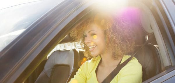 woman in yellow shirt smiling while driving black car