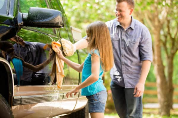 young girl washing black truck with dad