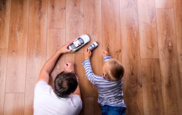 father plays with toy cars with his son on the hardwood floor of mobile home
