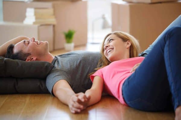 young renters hold hands while laying in new apartment