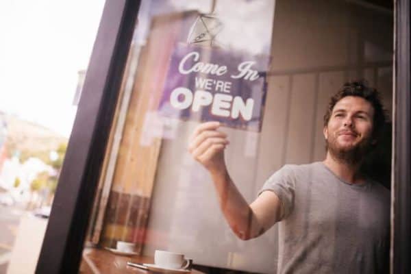 man hanging up a "we're open" sign for his business