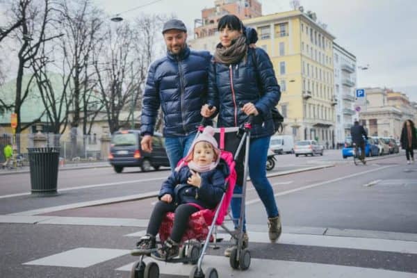 young family takes a walk in the city with child in pink stroller