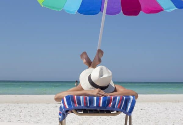 Woman relaxing on beach in beach chair with umbrella.