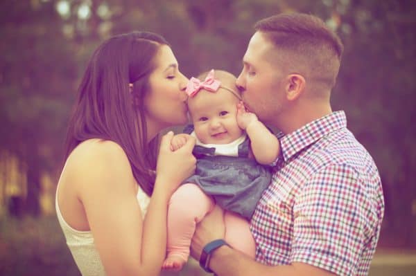 Parents hold their young child and kiss her on the head.