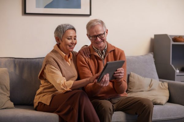 an elderly couple smiles as they read an iPad together